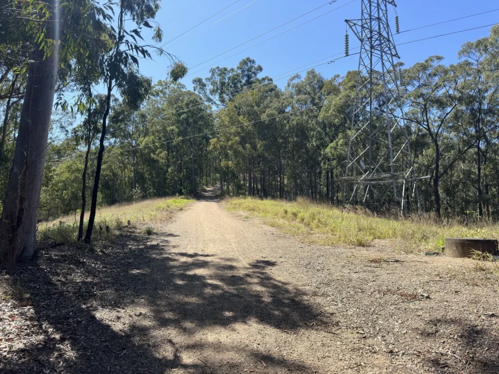 Ferny Hills dog walking trail with wide gravel path under powerlines beside bushland, showing one of the quiet local walking routes used by Furfolk dog walkers.