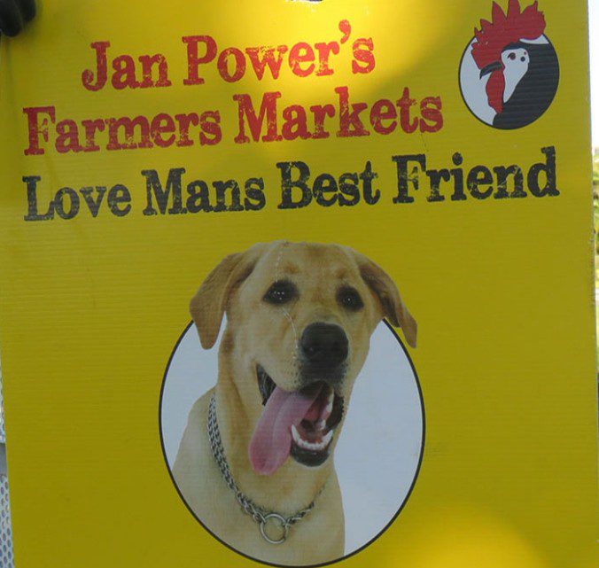 Yellow sign at Jan Powers Farmers Markets showing a dog illustration and the message “Love Man’s Best Friend”